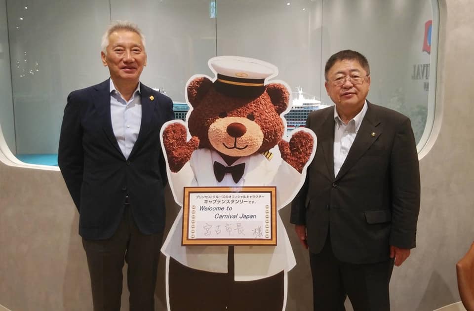 クルーズ客船ダイヤモンド・プリンセスのマスコットのスタンリーのパネルの両脇に、カーニバル・ジャパンの堀川悟代表取締役社長と市長が立って写っている記念写真