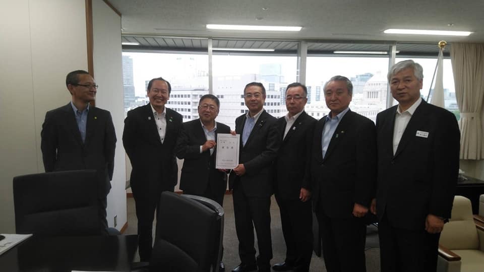 窓際で要望書を一緒に持つ市長と男性1名を中心に、関係者の男性5名が横一列に並ぶ記念写真