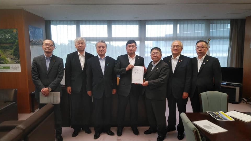 右から3番目と4番目の男性が要望書を持ち市長と関係者の男性6名が横一列に並んでいる記念写真