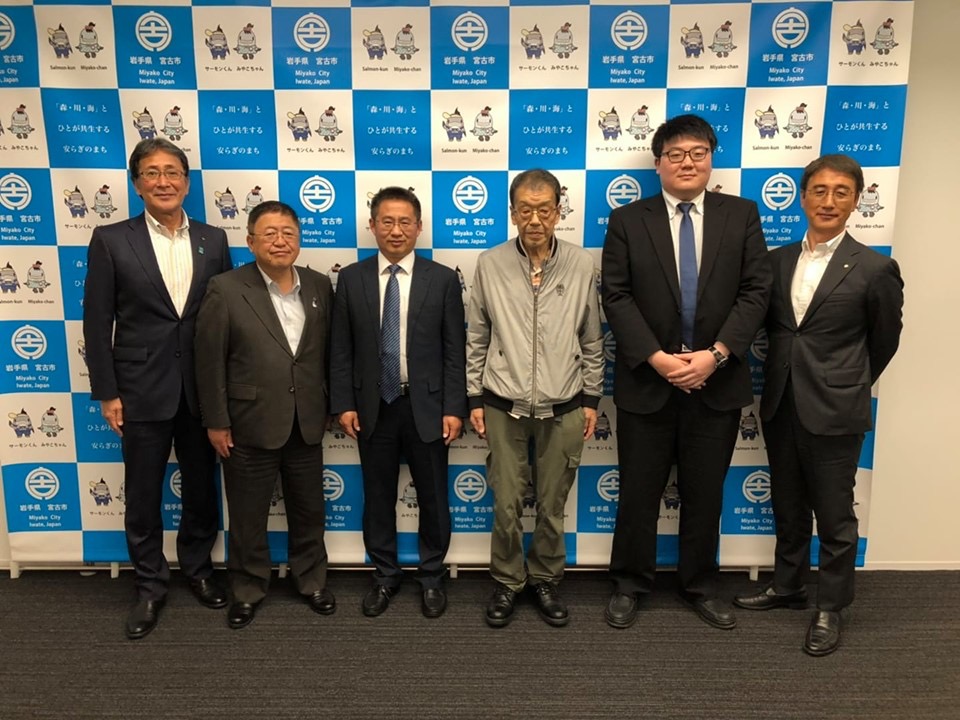 バックパネルの前で横一列に並んで記念撮影をする市長と関係者6名の写真