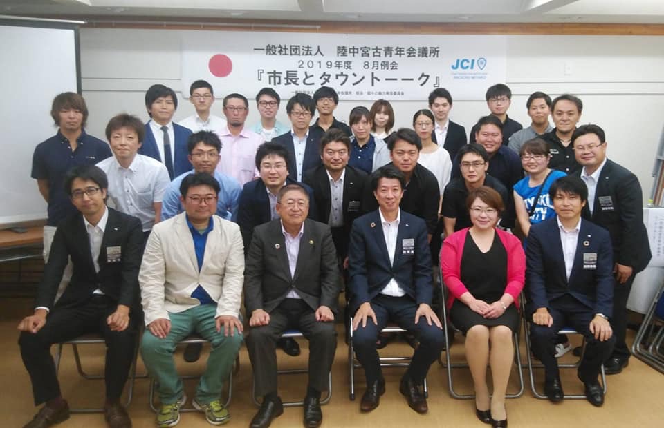 「市長とタウントーク」と書かれた横断幕が貼られた会場で、市長と参加者の方々が椅子に座ったり中腰になったりして4列になって並んでいる記念写真