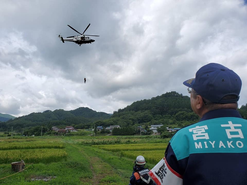 田んぼの上空を防災ヘリが飛んでいる様子を見ている市長の後ろ姿の写真