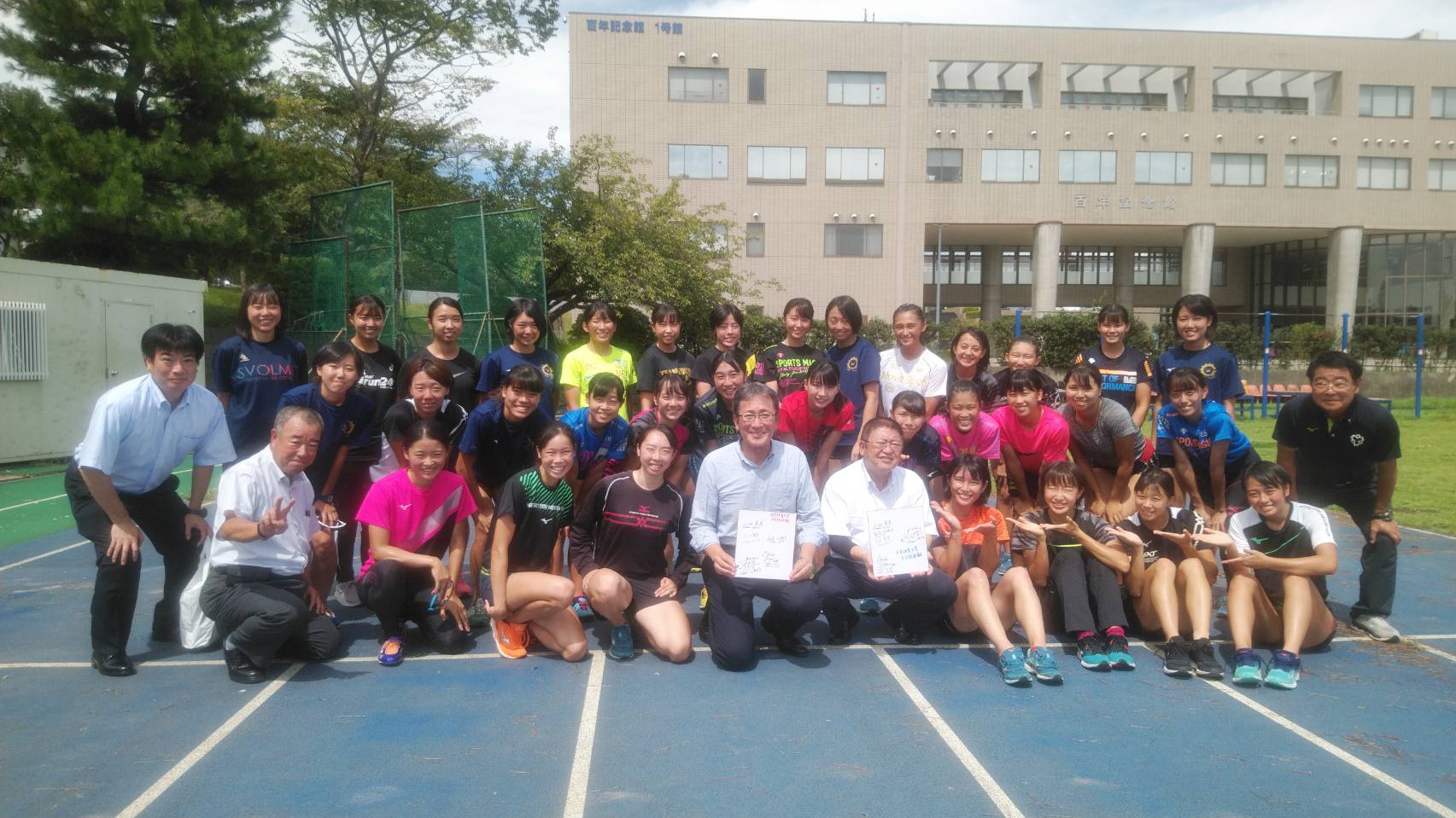 寄せ書きを持った市長と大村邦英先生を中心に日本体躯大学陸上競技部の方々が集まった集合写真