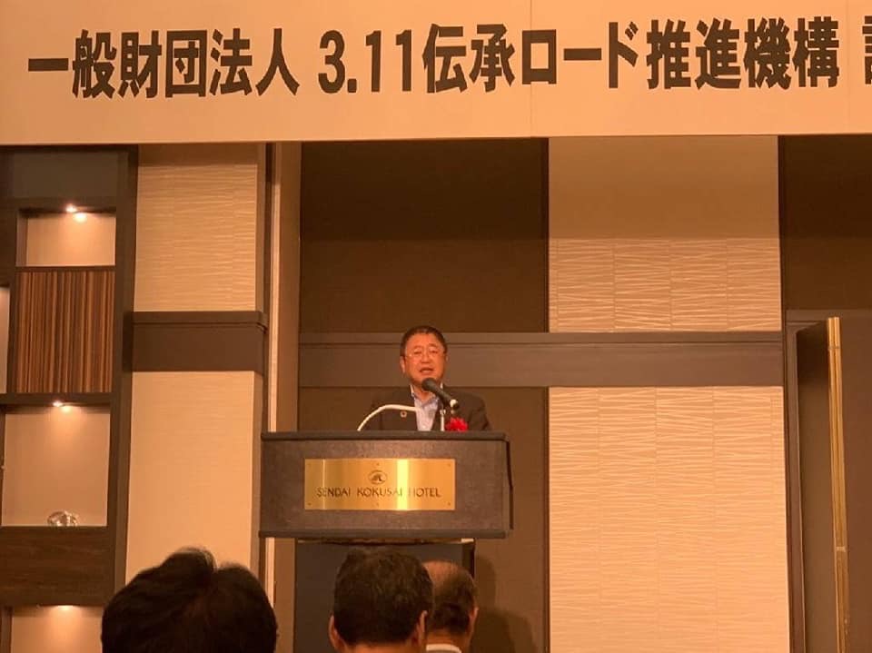 スーツに胸章を付けた市長が壇上に立ち話をしている様子の写真