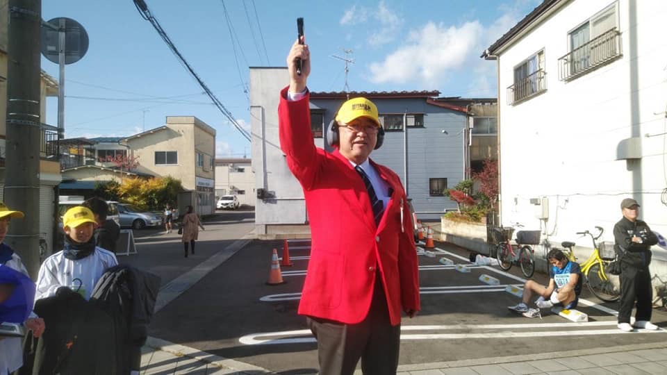赤いジャケットを着て黄色い帽子を被り、右手に持ったピストルを頭上に掲げている様子の市長の写真