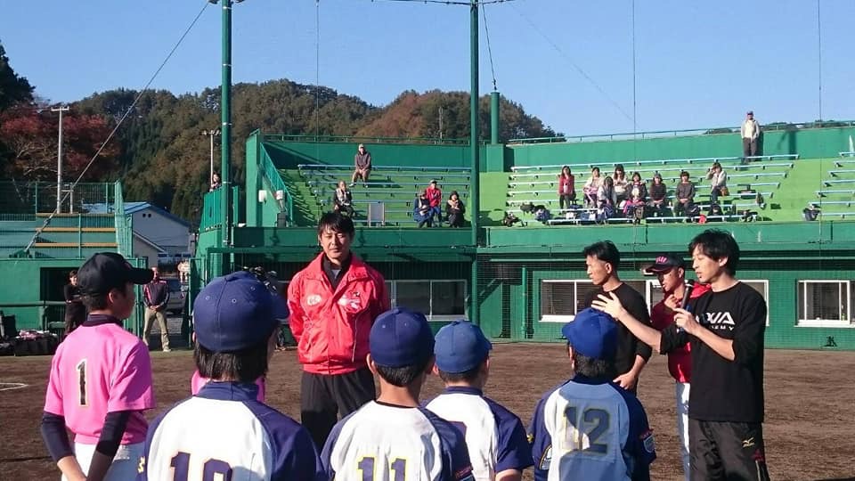 野球場で岩隈久志GMとユニフォームをきた子供たちが写る写真
