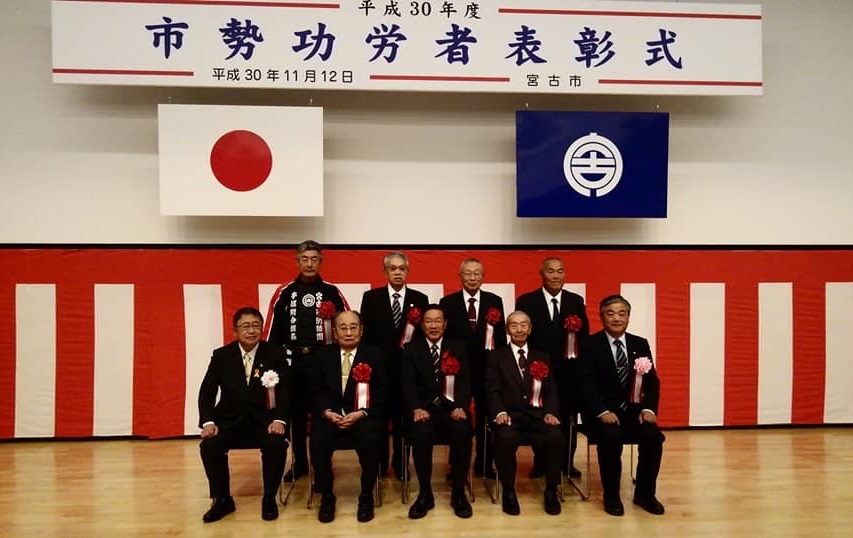 「市勢功労者表彰式」と書かれた横断幕と日本国旗、宮古市の市町村旗が掲げられた会場で、前列に椅子に座った市長と4名の方が並び、後列に4名の方が立って並んでいる記念写真