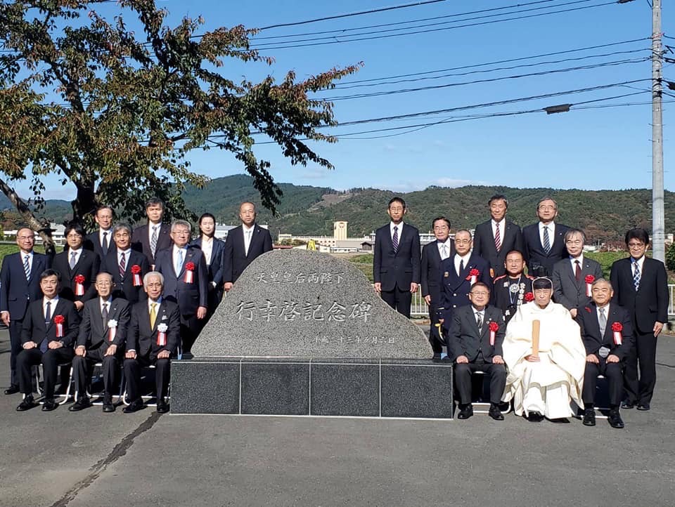 記念碑の周りに集まって記念撮影をしているスーツを着た関係者の方々と祭服を着た方の写真