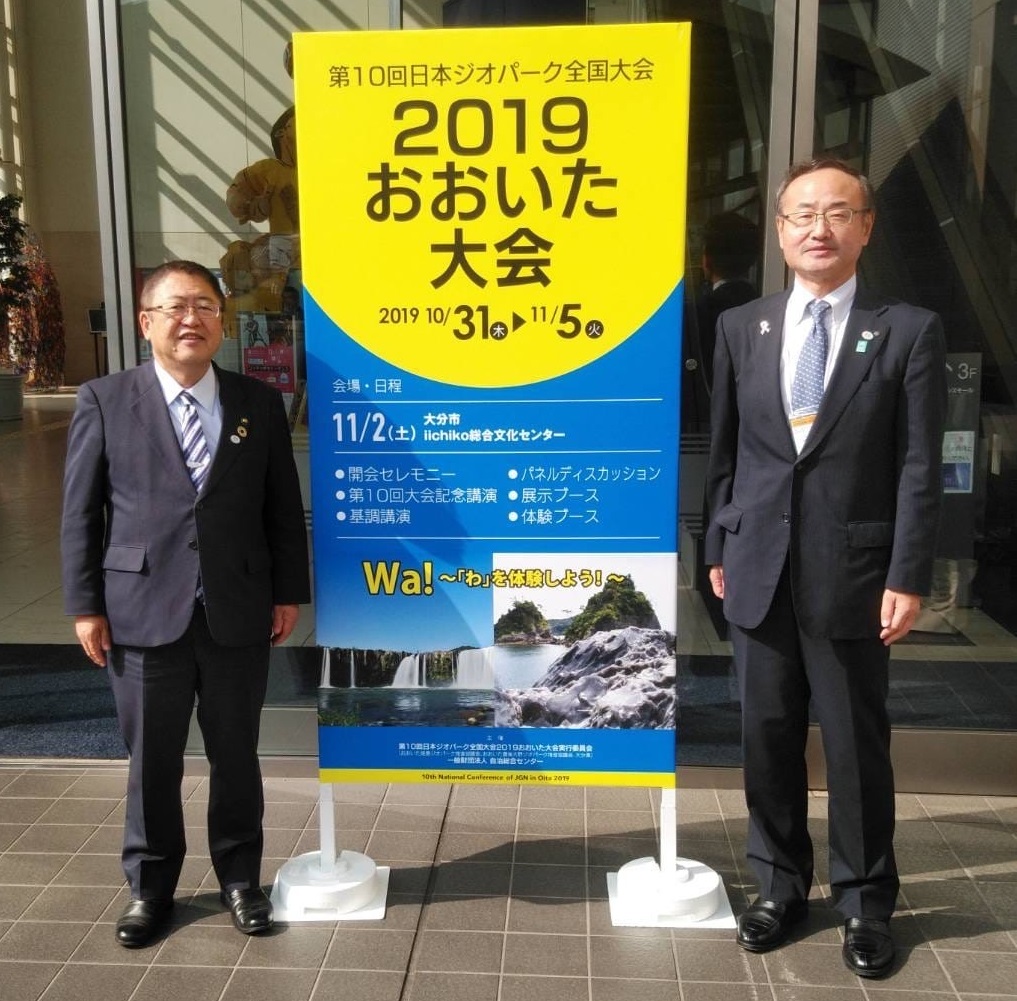 「第10回日本ジオパーク全国大会2019おおいた大会」と書かれた看板を中心に、市長と県の関係者が写る記念写真