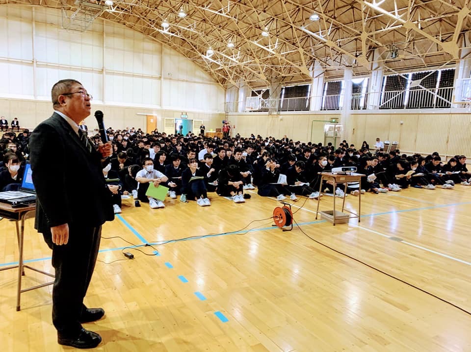 体育館の床に体育座りをして整列する宮古高等学校の学生たちと、マイクを持って立ちながら話をする様子の市長の写真