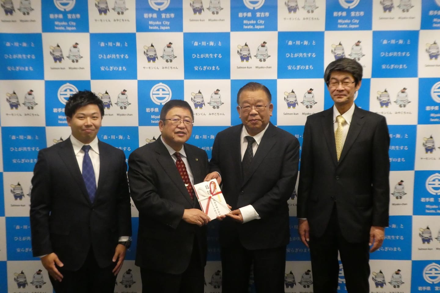 目録を一緒に持つ市長と男性を中心に、関係者の男性2名が横一列に並んでいる記念写真