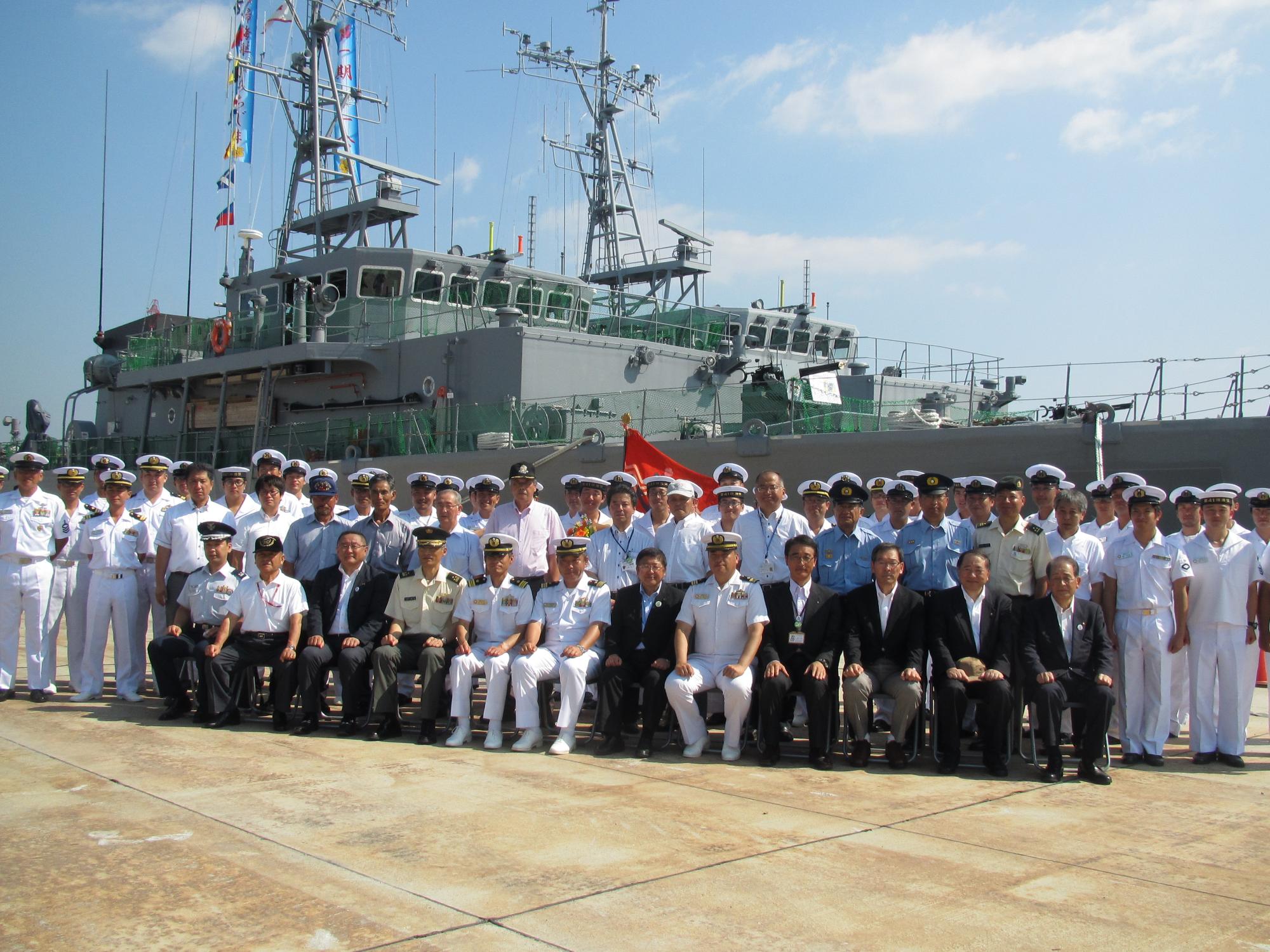 海上自衛隊掃海艇の前で整列する海上自衛隊員と椅子に座る市長や関係者の方々の記念写真