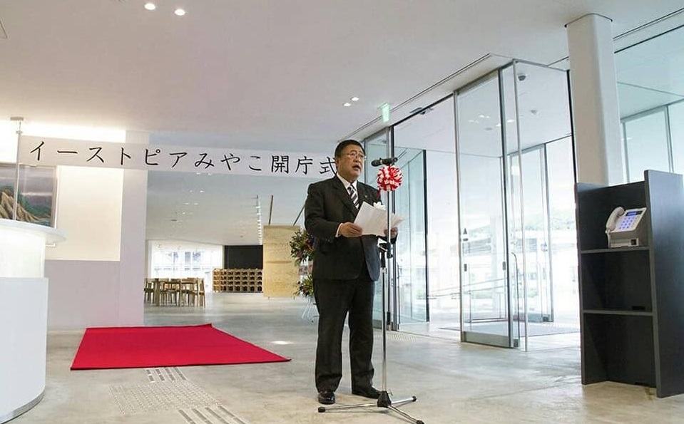 式辞用紙を両手で持って、紅白リボンがついたスタンドマイクに向かい話をする様子の市長の写真