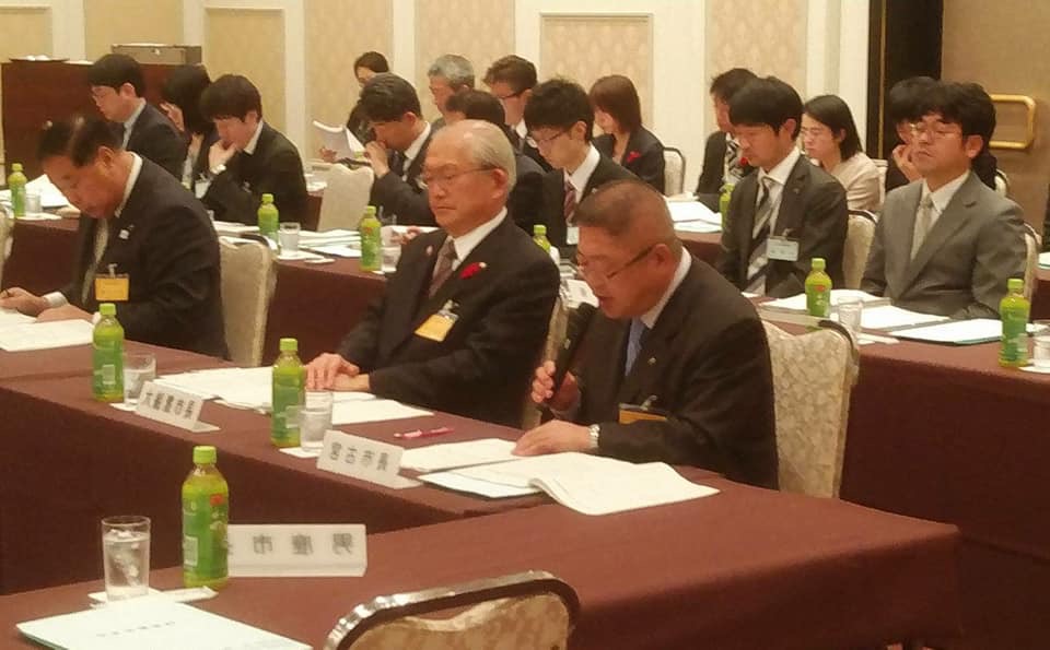長机に2名ずつ出席者の方々が座っている中、市長が自席で資料を見ながら、マイクで話をしている写真
