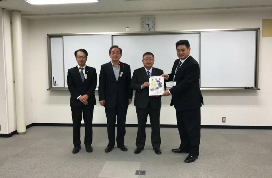 ホワイトボードの前で、要望書を一緒に持つ市長と男性と関係者2名の男性が横一列に並んでいる記念写真