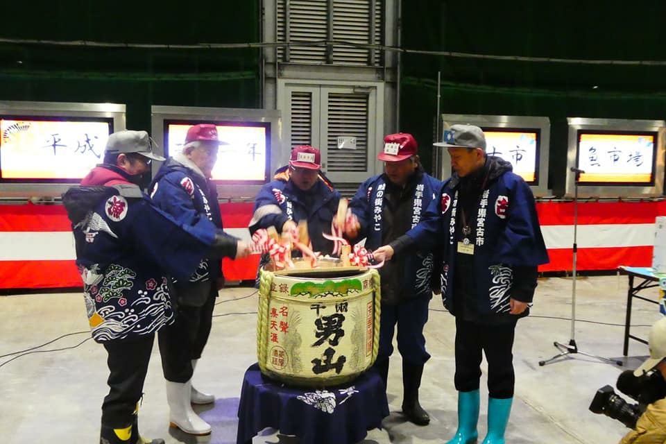 法被にキャップを被った市長と4名の関係者が木槌を持ち、酒樽の周りを囲んで鏡開きを行っている初売り式の様子の写真