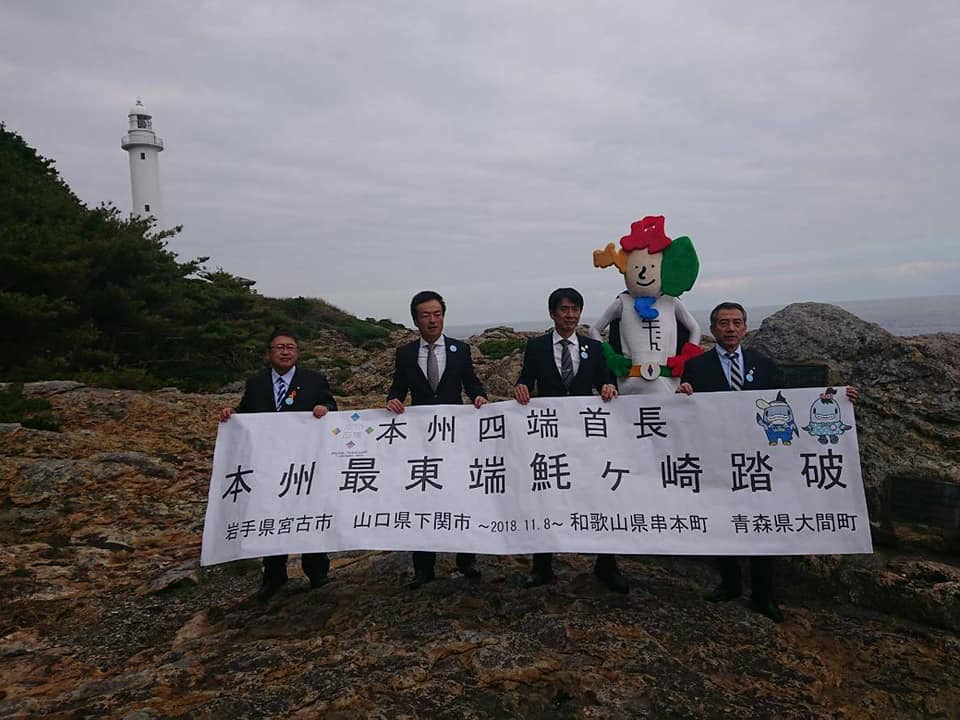 「本州四端首長 本州最東端魹ヶ崎踏破」と書かれた横断幕を持つ山口県下関市の前田晋太郎市長、和歌山県串本町の田嶋勝正町長、青森県大間町の金澤満春町長と山本市長の写真
