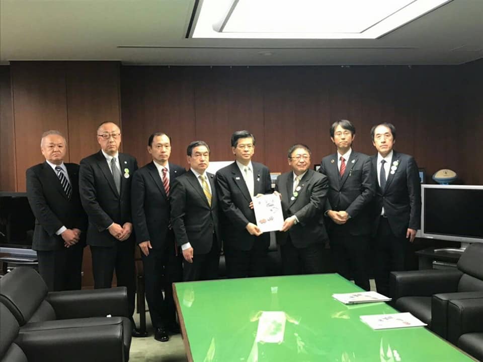 長机の奥で要望書を一緒に持つ市長と男性を中心に、関係者の男性6名が横一列に並んでいる記念写真