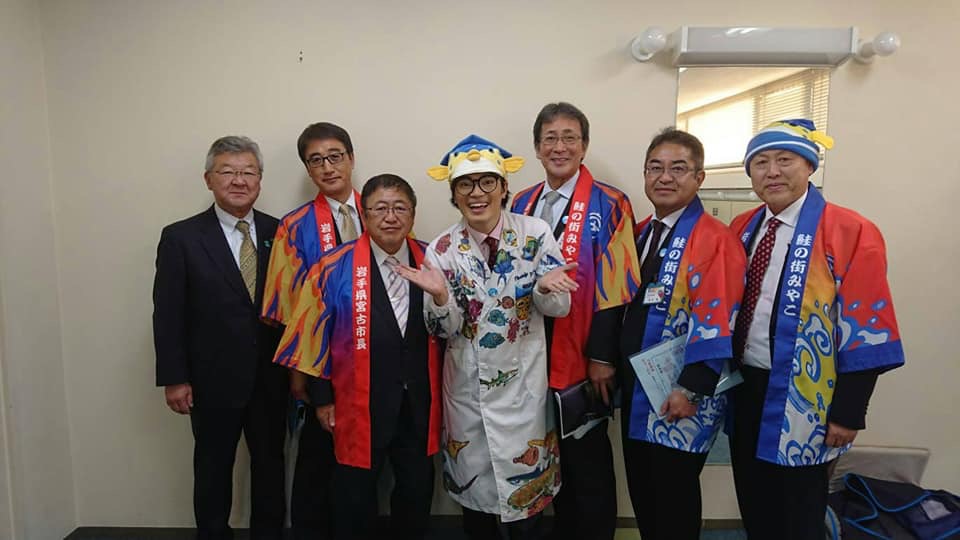 両手を広げたさかなクンを中心に市長と関係者の男性5名が横一列に並んでいる記念写真