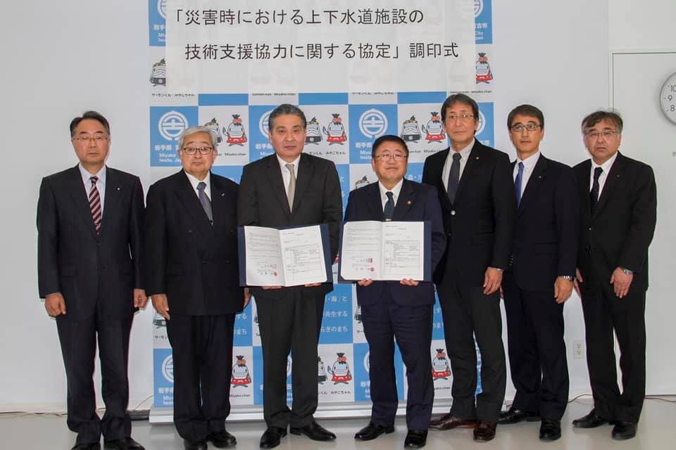 協定書を広げて持つ市長と男性を中心に、関係者の男性5名が横一列に並んでいる記念写真