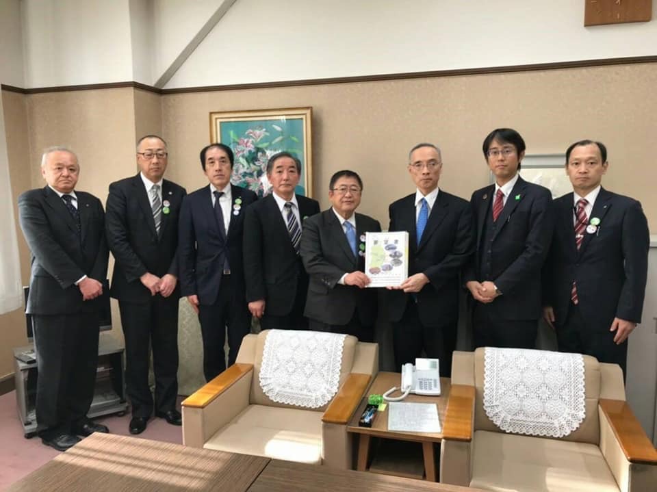 応接室内で要望書を一緒に持つ市長と男性を中心に、関係者の男性6名が横一列に並んでいる記念写真
