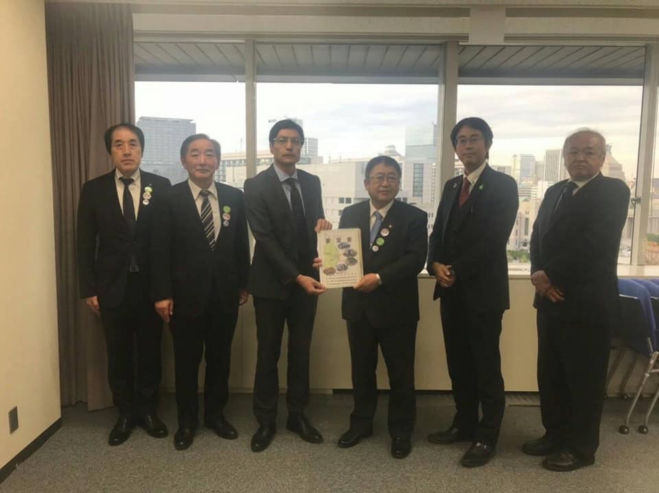 窓際で要望書を一緒に持つ市長と男性を中心に、関係者の男性5名が横一列に並んでいる記念写真