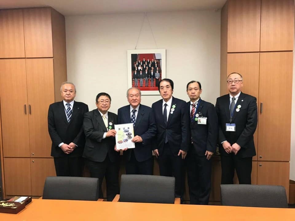 椅子の奥で要望書を一緒に持つ市長と男性と関係者の男性4名が横一列に並んでいる記念写真