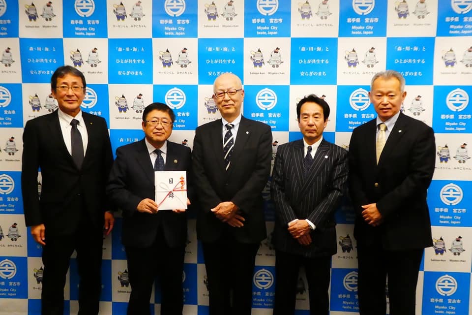 バックパネルの前で目録を持つ市長と株式会社ユニバースの関係者の方々が横一列に並んでいる記念写真
