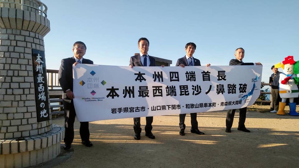 「本州四端首長 本州最西端毘沙ノ鼻踏破」と書かれた横断幕を持つ山本市長と下関市の前田市長、串本町の田嶋町長、大間町の金澤町長の記念写真