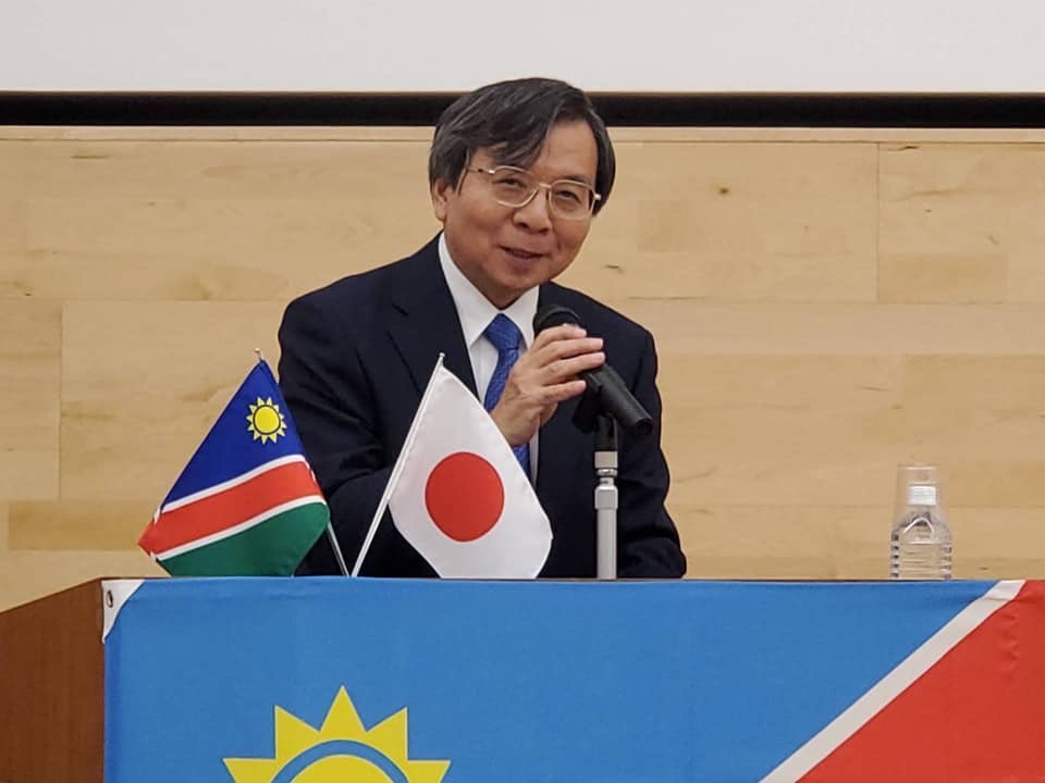 小さい日本国旗とナミビア国旗が置かれた演台で話をする様子の在ナミビア共和国大使館原田秀明全権大使の写真