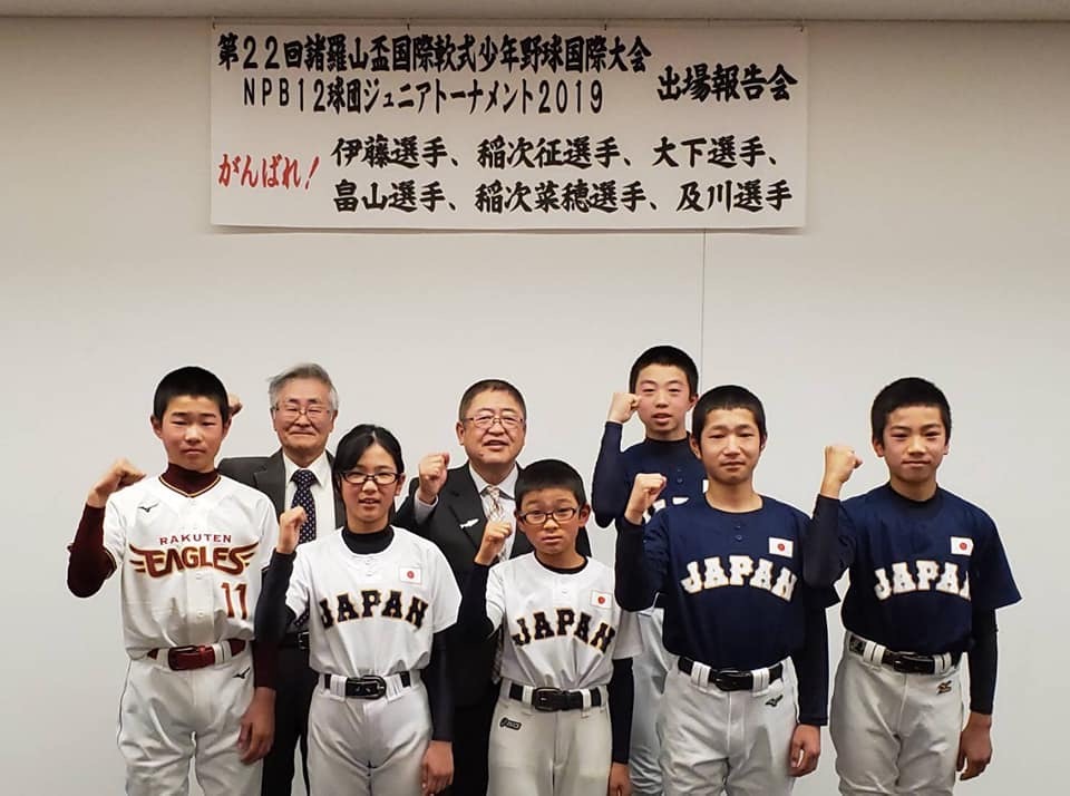 野球のユニフォームをきた小学生の男女6名と、市長、関係者の男性1名が右腕を曲げ握りこぶしを顔の横に掲げてポーズをとり2列に並んで立っている記念写真