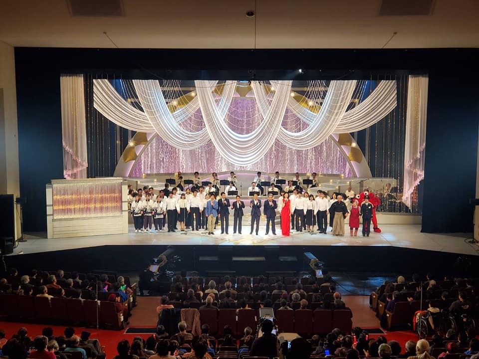 コンサート会場の舞台に出演者が集合している写真