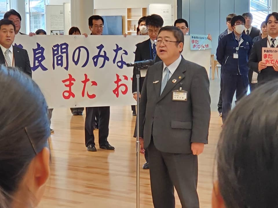 スタンドマイクの前で立って話をする様子の市長と、周りで横断幕を持って立つ関係者達の写真