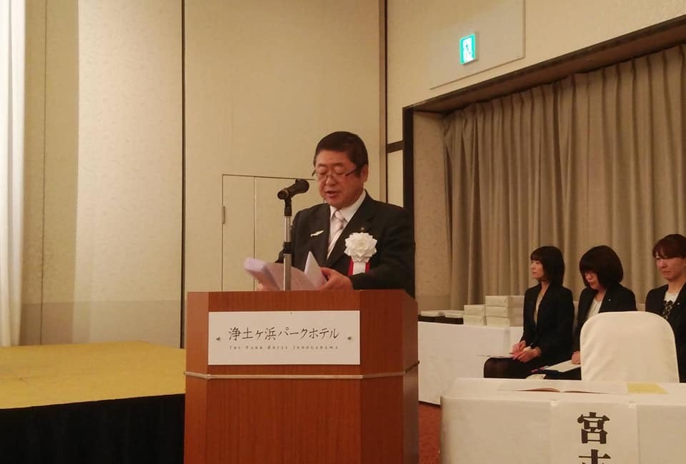 演台の前で白い胸章を着けた市長が式辞用紙を見ながら話をしている様子の写真