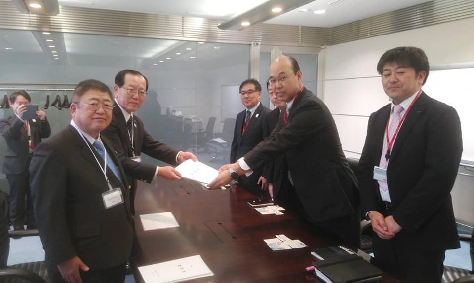 NTTドコモ東北支社の部長と3名の関係者、細長いテーブルを挟んで向かい合って立つ市長と並んで立っている本田遠野市長が一緒に要望書を持っている写真