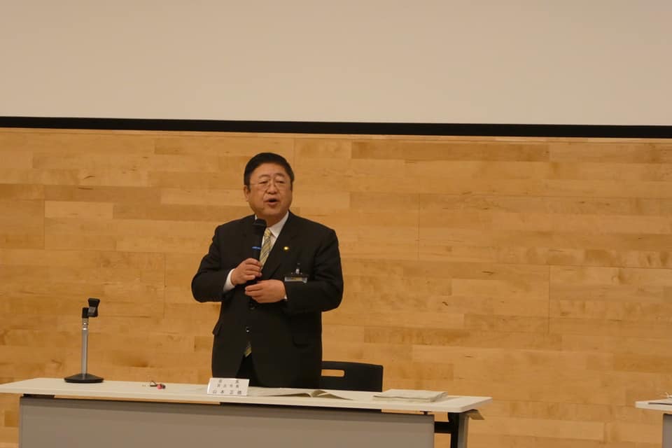 長机の席から立ち上がった市長が、右手にマイクを持ち話をしている会議の様子の写真