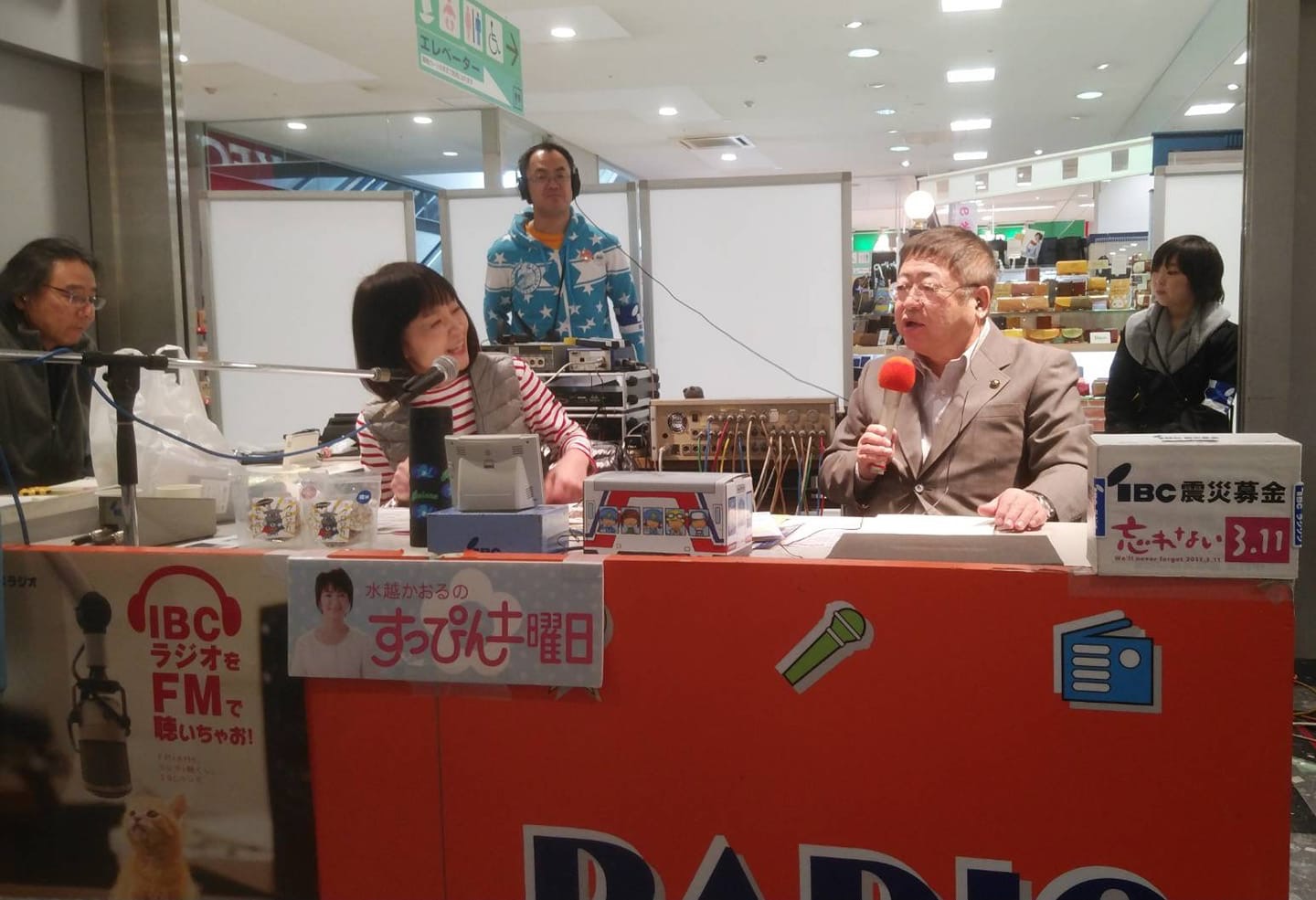 ショッピングセンターの一角に設けられたラジオの公開生放送のブースに水越かおるさんと市長が座り、右手にマイクを持った市長が宮古市のPRを行っている様子の写真