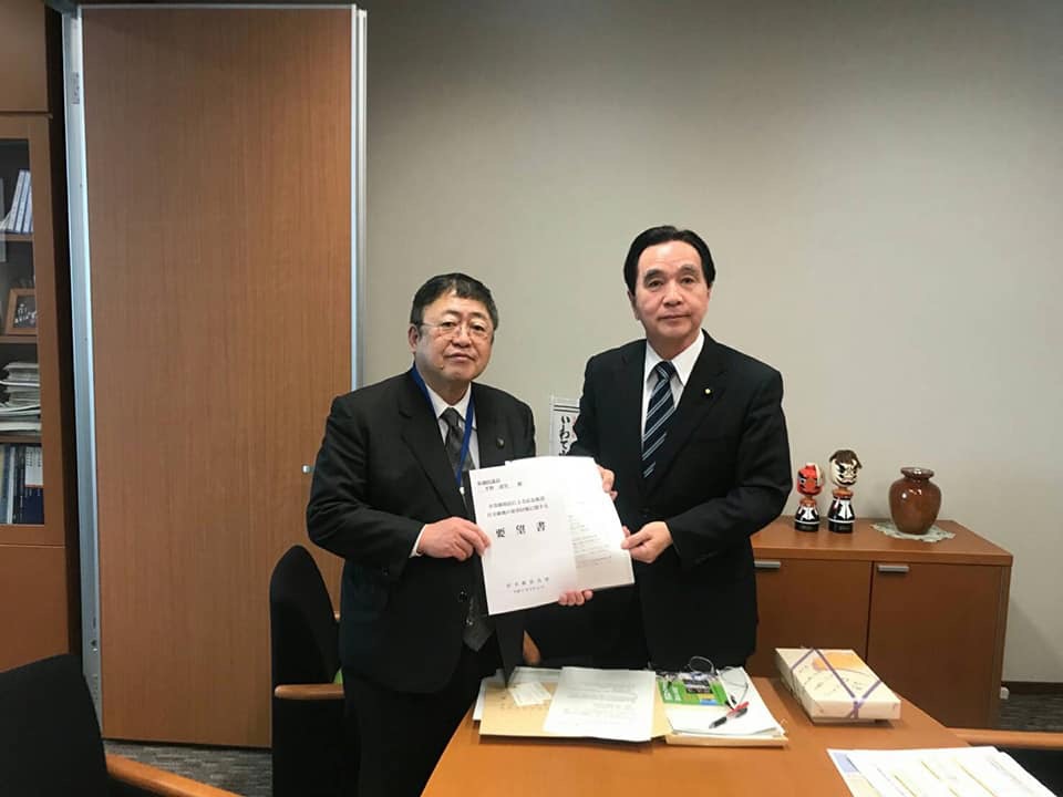 テーブルに資料が置かれた室内で、男性と市長が一緒に要望書を持っている写真