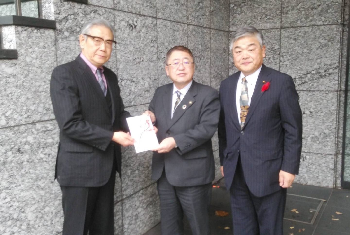 義援金の封筒を一緒に持つ男性と市長の隣に男性が1名立ち並んでいる記念写真