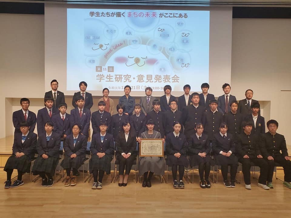 画面が映されたスクリーンの前で、3列になって並び記念撮影をする学生と関係者たちの写真