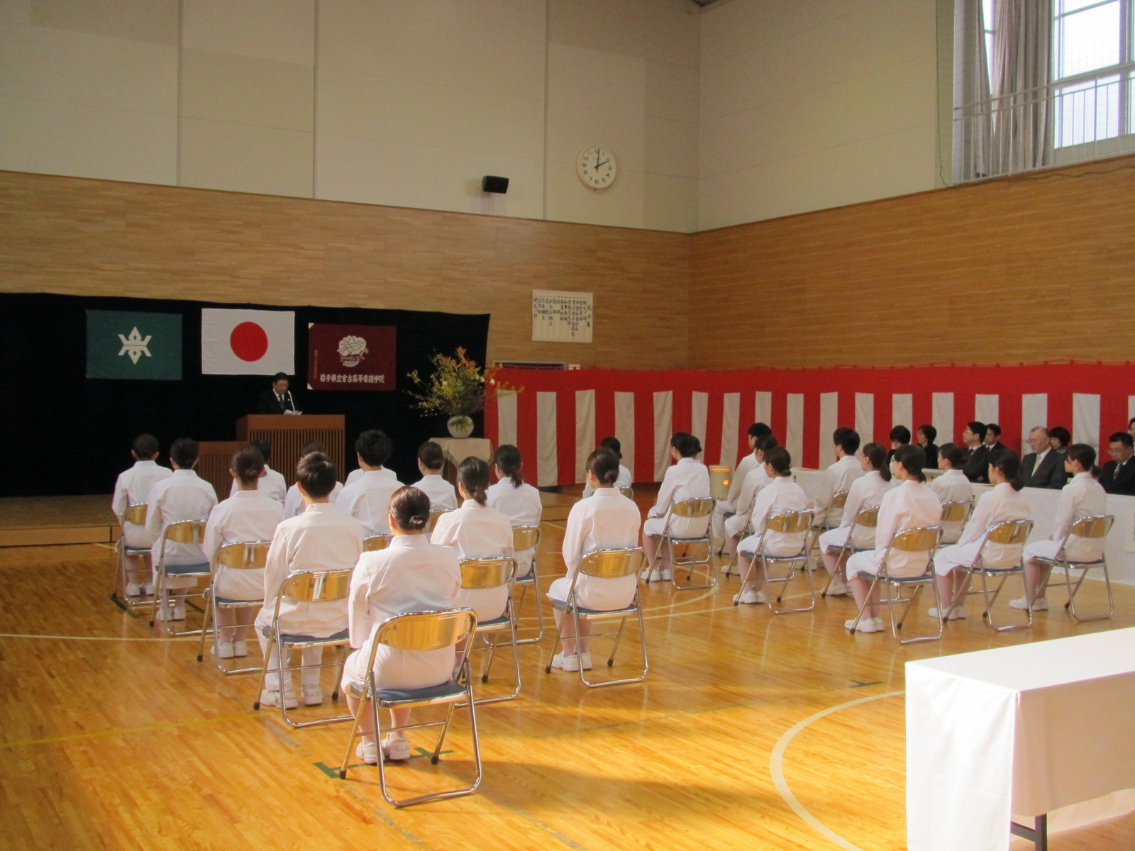白い制服を着てパイプ椅子に座った看護学生と、演台のマイクに向かい話をする市長の写真