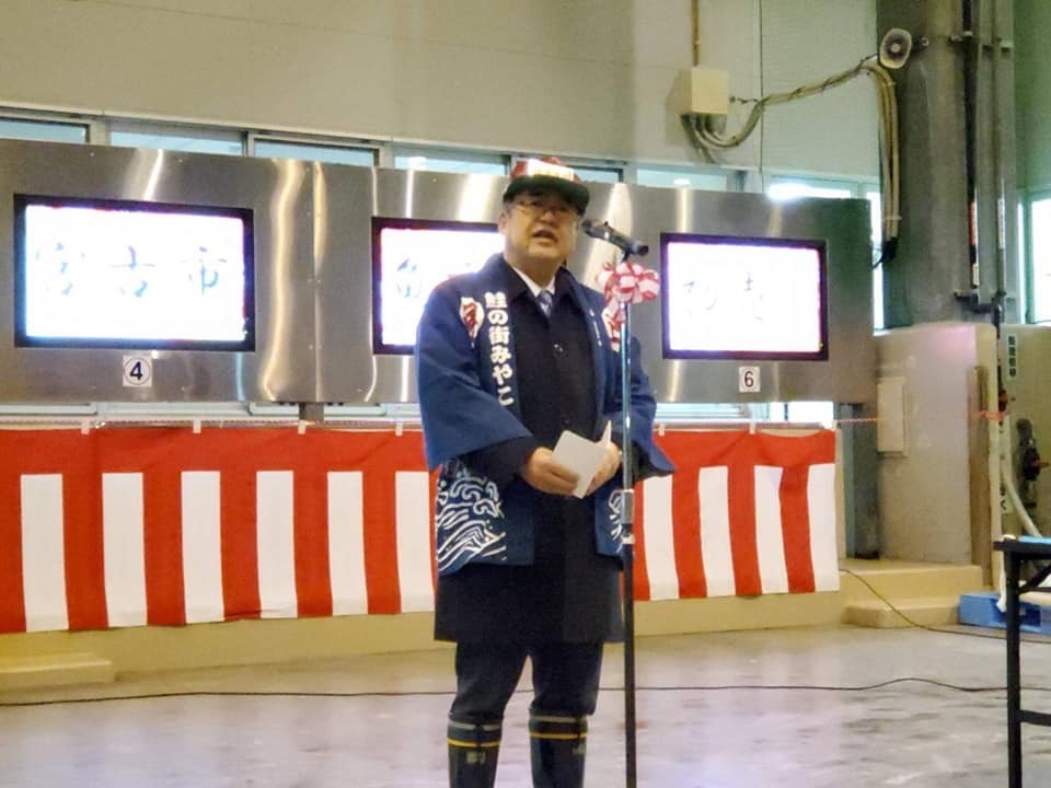 帽子を被り法被を着た市長が、市場に置かれたスタンドマイクに向かい話をする様子の写真