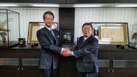 奥に賞状が飾られた室内で、両手で握手している男性と市長の写真