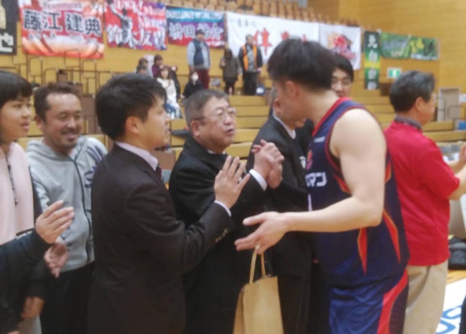 ユニフォームを来た選手と握手する市長と、その周りで選手を見ている関係者の方々の写真