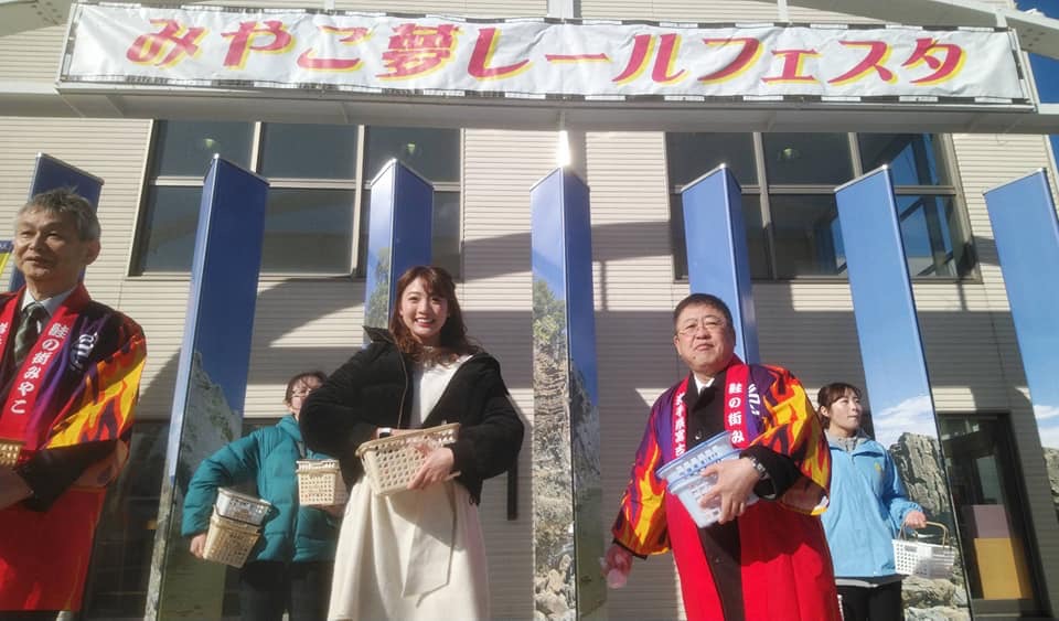 「みやこ夢レールフェスタ」と閣下れた横断幕が掲げられた会場で、法被を着た市長や関係者の男性、黒いジャケットを着た女性などが餅まきをする様子の写真