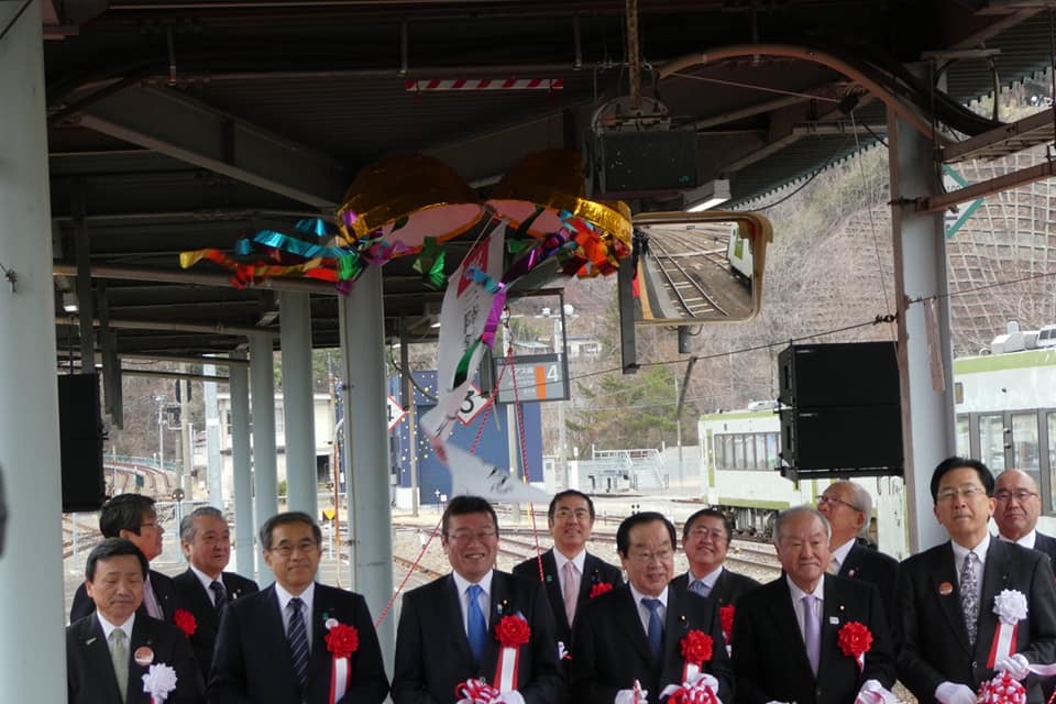ホームの天井から吊るしてある割られたくす玉の下で、胸章を着けた三陸鉄道リアス線開通記念列車出発式の参加者たちが整列している写真