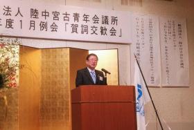 金屏風の前に置かれた演台で、マイクに向かって話をする様子の市長の写真