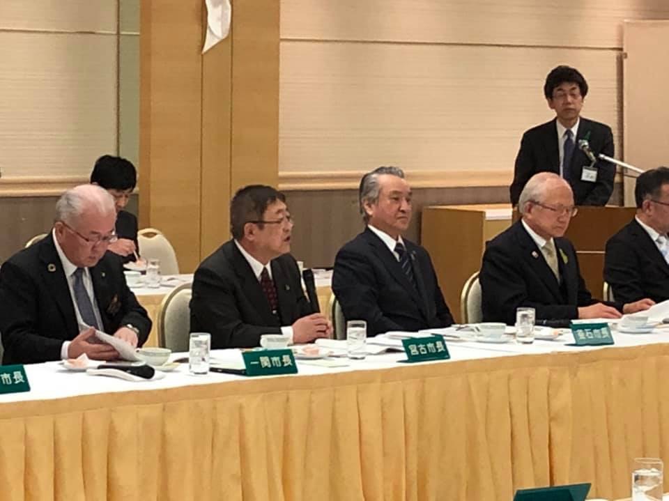 クロスが敷かれたテーブルに並んで座る5名の各市の市長たちの中心で、マイクを持ち話をしている様子の市長の写真