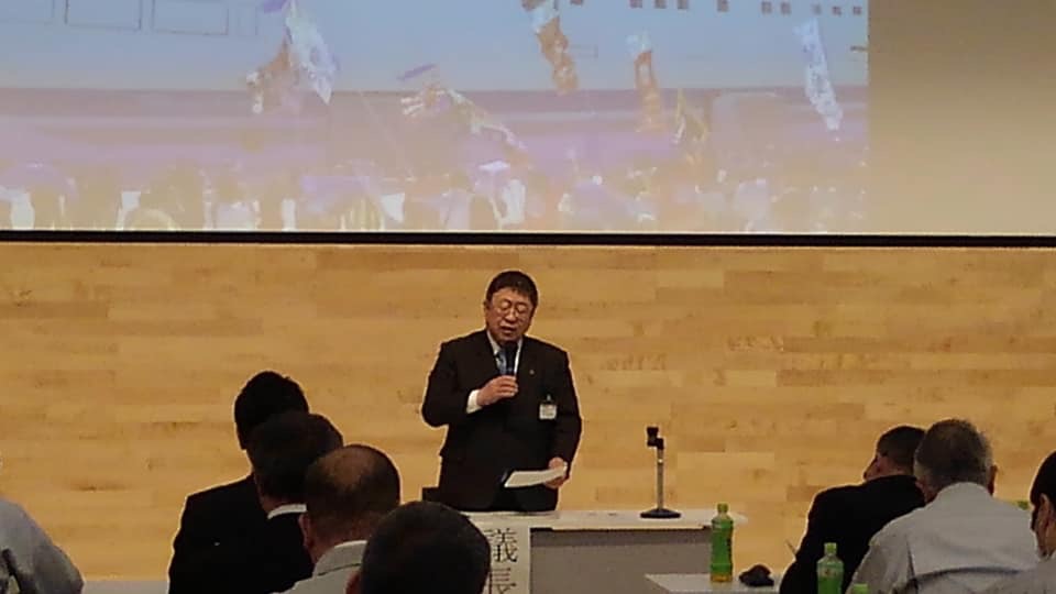 画像が映されたスクリーンの前で、右手にマイク、左手に資料を持ち話をしている様子の市長の写真
