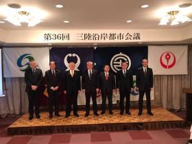 第36回三陸沿岸都市会議と書かれた幕の下で、会議に出席した7市の市長の方々が、ステージ上に並んで撮影した写真